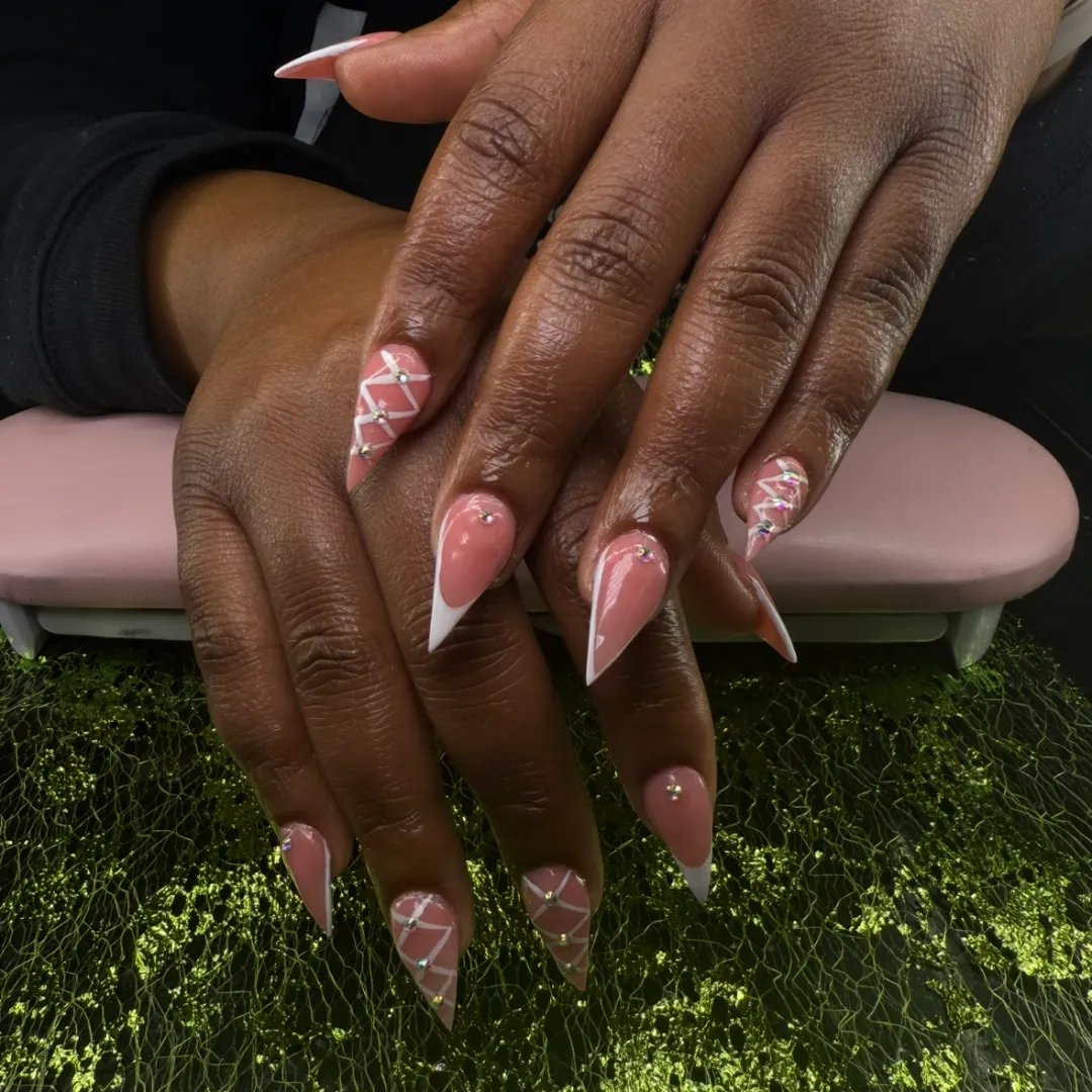 Pink stiletto nails with white geometric line art and crystals